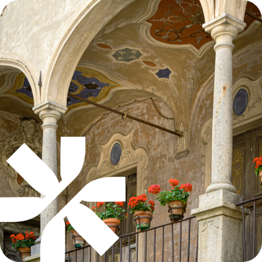 Porticato storico con archi affrescati, colonne in pietra e balconata fiorita