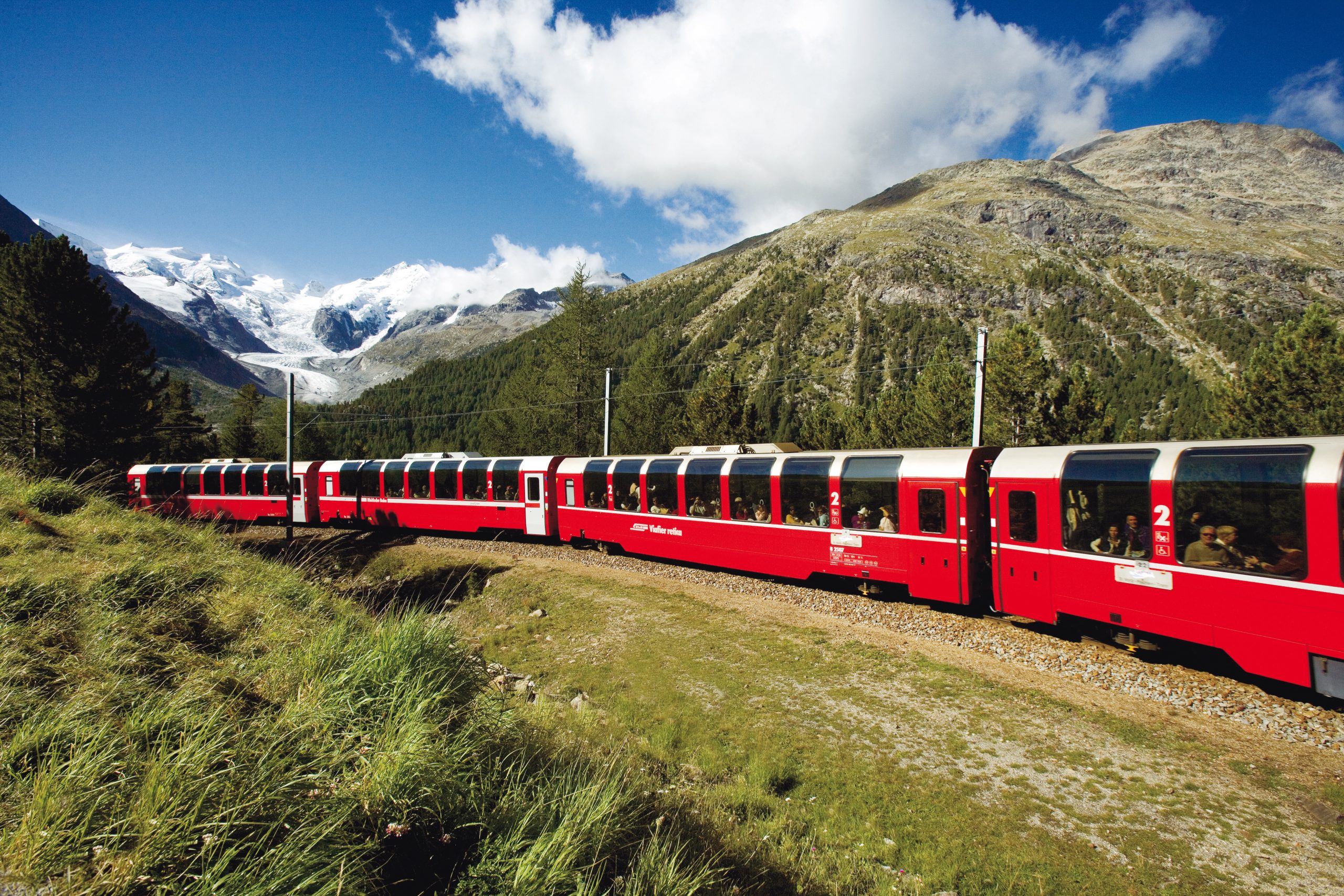 Treno rosso panoramico che attraversa paesaggio alpino con ghiacciaio sullo sfondo