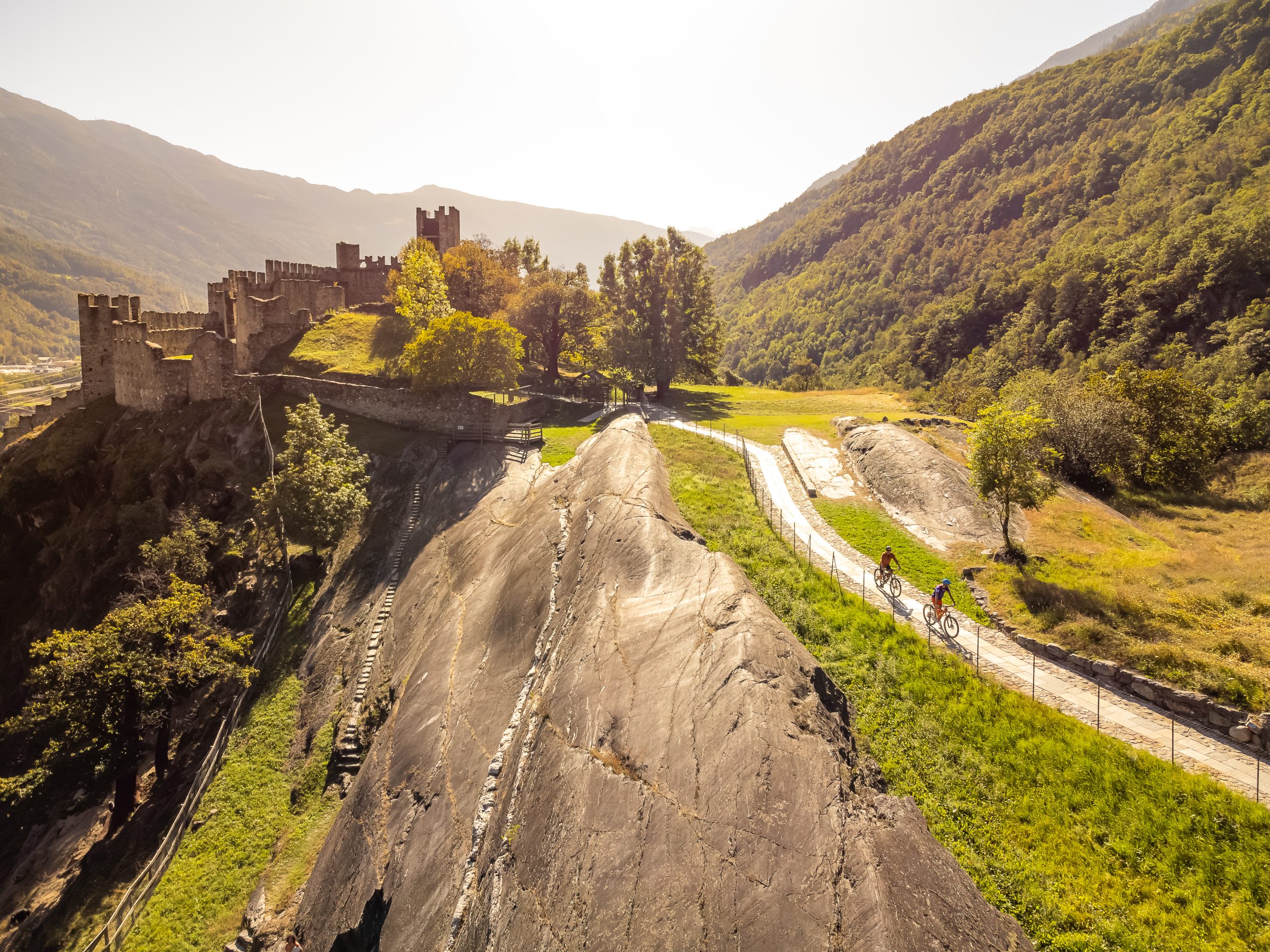Ciclisti su percorso panoramico accanto a un castello medievale in valle montana