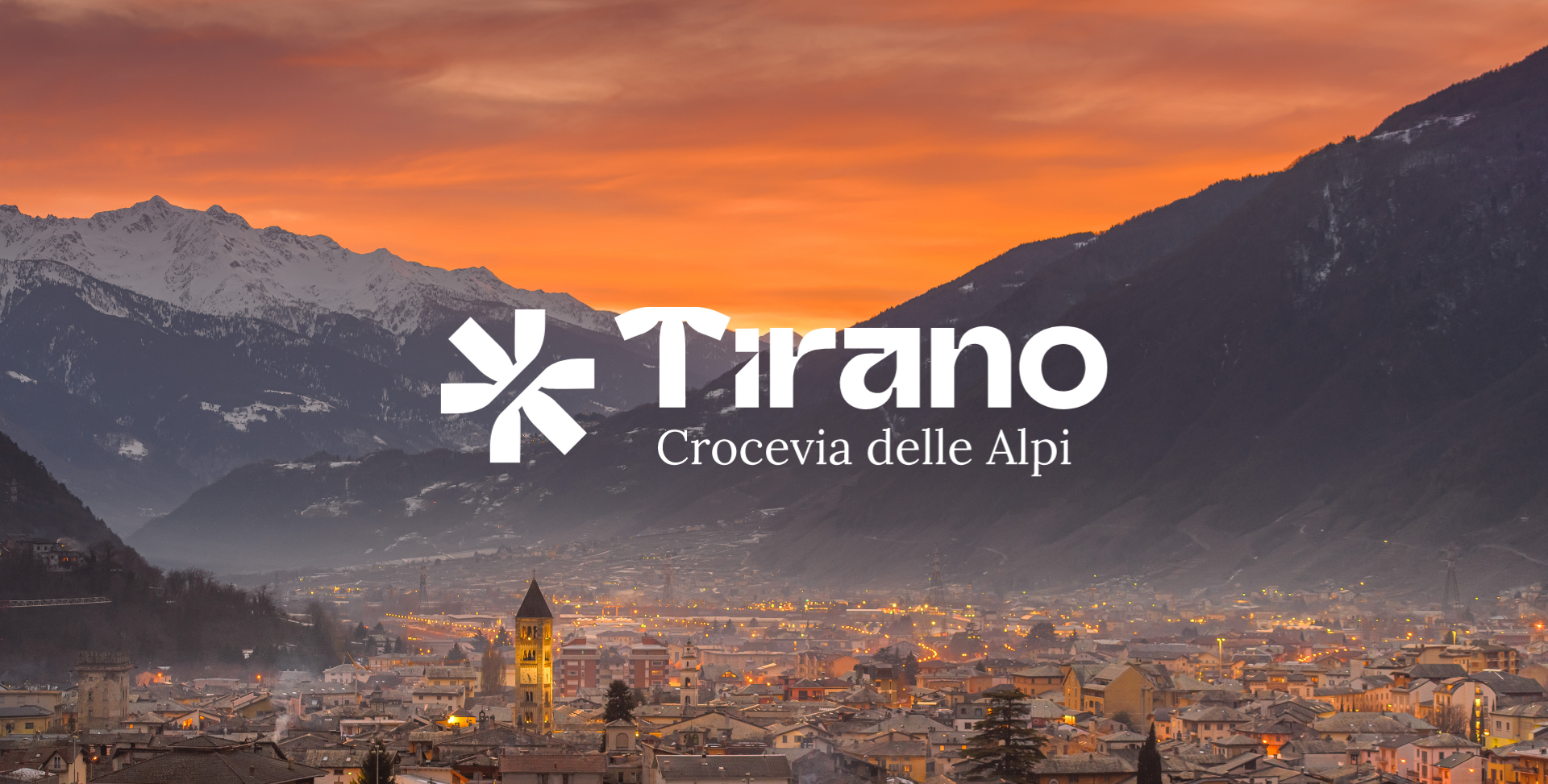Vista panorámica de Tirano al atardecer con montañas alpinas y cielo naranja