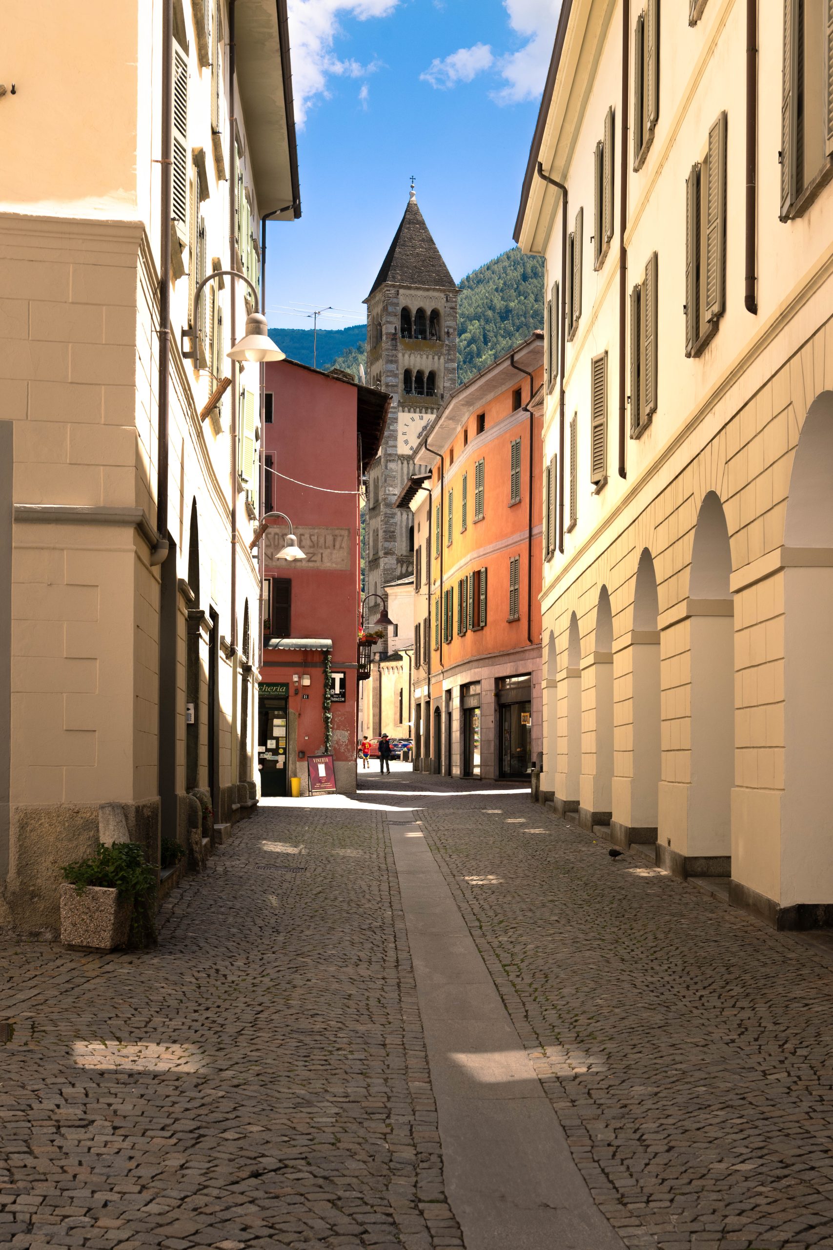 Calle del centro histórico con edificios coloridos y campanario de piedra al fondo en una pequeña ciudad alpina